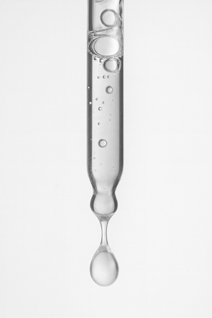 Close-up of a clear hair oil droplet forming on a glass dropper, highlighting lightweight, silicone free formula