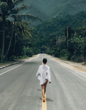 Person walking alone on a deserted road surrounded by lush greenery