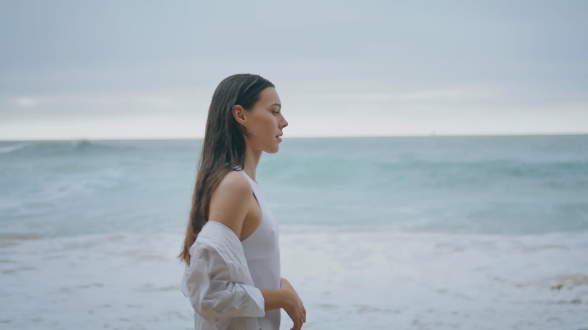 short video of woman walking along the ocean shoreline with wet, glossy hair, showcasing natural shine and movement after using silicone-free kluē reborn hair oil