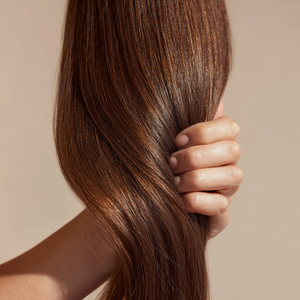 Hand holding silky, glossy brown hair to highlight strengthening and smoothing benefits of silicone free luxury hair oil